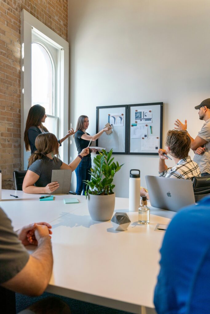 A business meeting with people standing in front of a whiteboard